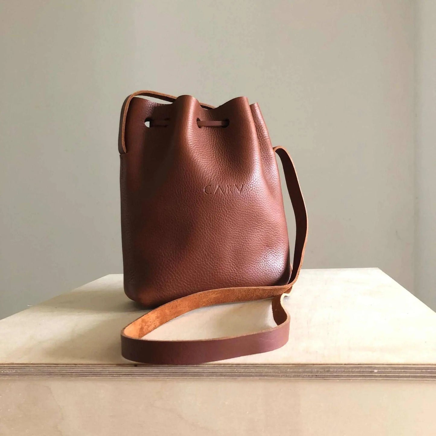 Nomad Small Leather Bucket Bag in tan brown with adjustable strap, handcrafted from vegetable-tanned leather, featuring a raised grain texture.