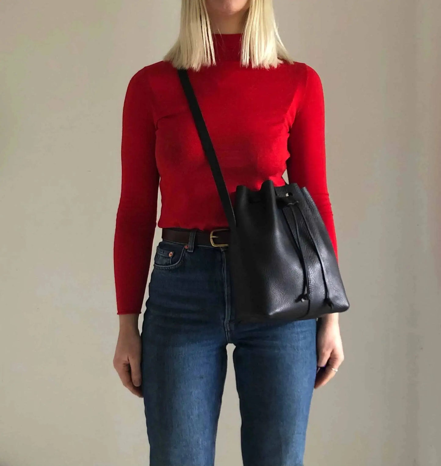 Nomad Midi Tan Leather Bucket Bag worn crossbody, showcasing minimalist style and adjustable strap.