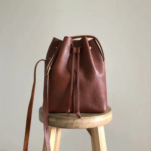 CARV tan leather bucket bag sat on wooden stool