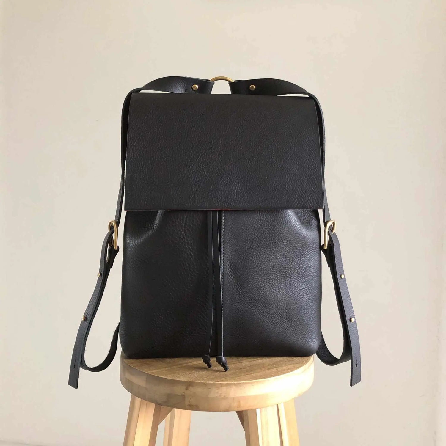 Nomad black leather backpack with squared minimalist flap standing on a wooden stall.