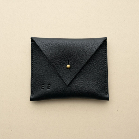 Black leather cardholder with gold accent on a beige background